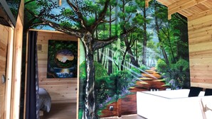 Una habitación con un amplio mural de un paisaje forestal, vigas de madera en el techo y una cama con vistas al mural.