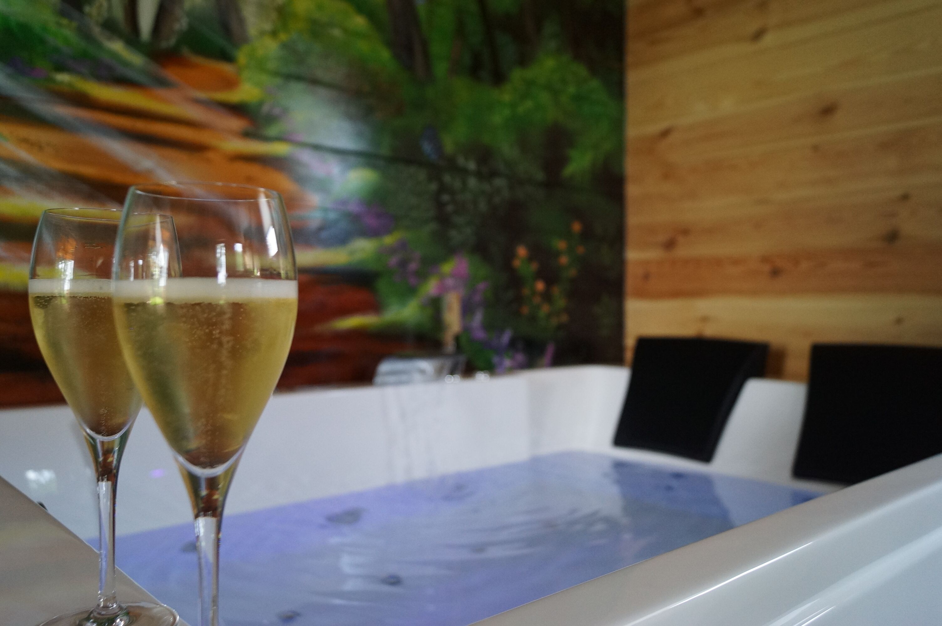 Two champagne glasses on a table with a wooden wall and a mural in the background.