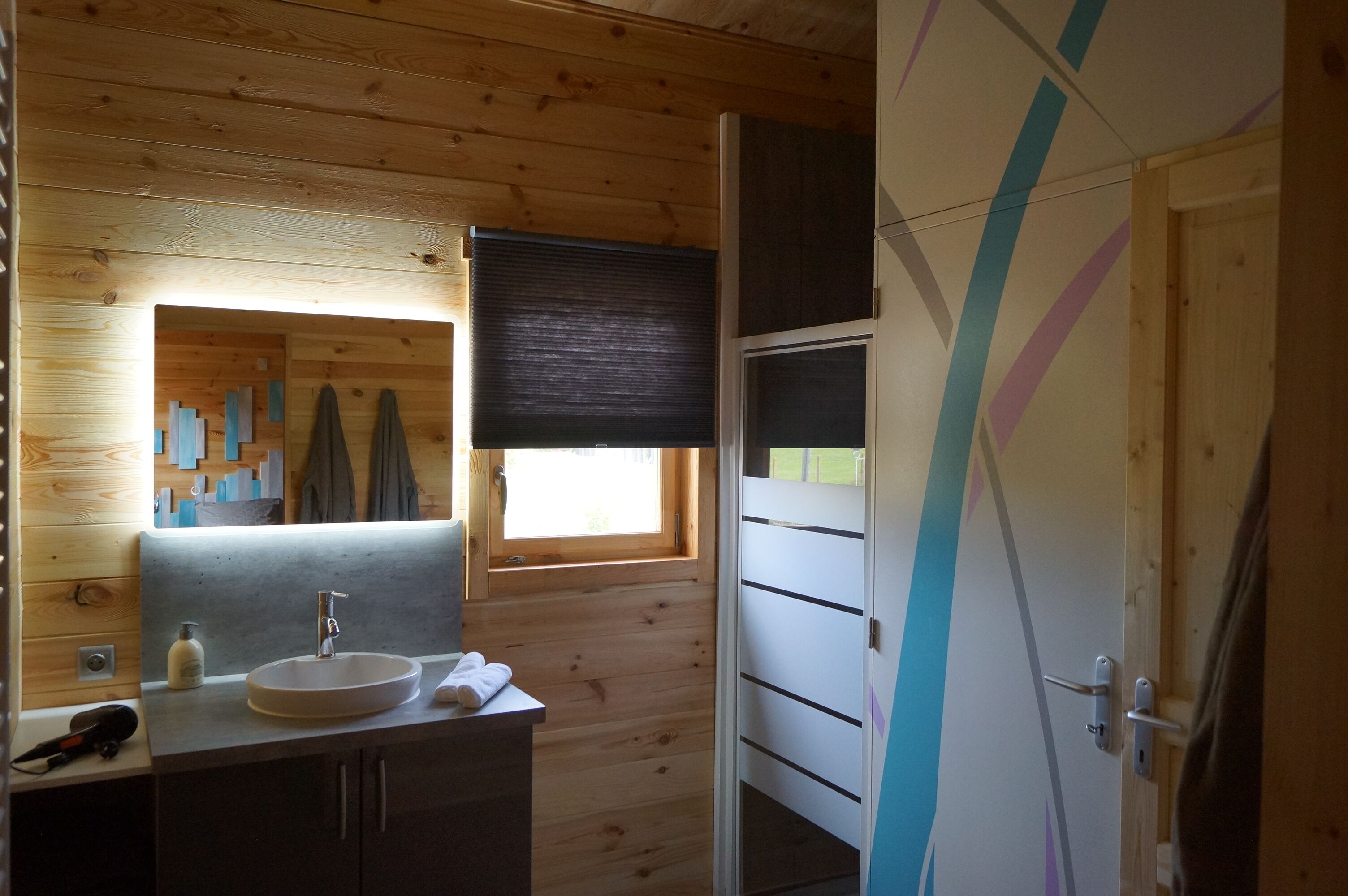 Un baño tipo cabaña de madera con lavamanos, espejo y perchero para toallas.