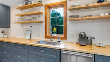 A kitchen with wooden shelves, a window, a sink, and a coffee maker.