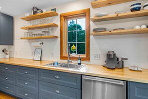 Une cuisine avec des étagères en bois, une fenêtre, un évier et une machine à café.