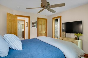 Un dormitorio con cama, ventilador de techo, televisión y puertas de madera.