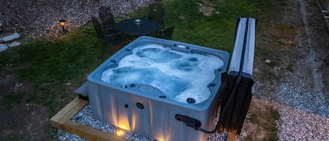 A hot tub on a wooden platform with a table and chairs nearby.