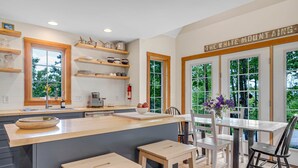 Una cocina moderna con estanterías de madera, una isla central y una zona de comedor con mesa y sillas.