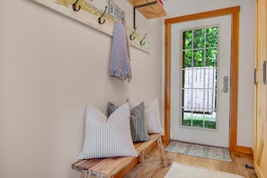 A wooden bench with striped pillows, a coat rack with a towel, and a door with a window view.