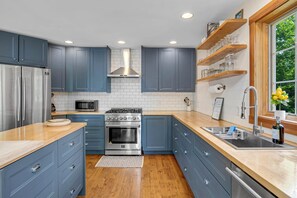 Een moderne keuken met blauwe kastjes, roestvrijstalen apparatuur en houten aanrechtbladen.