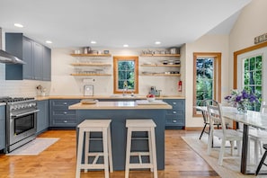 Una cucina moderna con mobili grigi, piani di lavoro in legno, una penisola centrale con sgabelli e un'area pranzo con tavolo e sedie.
