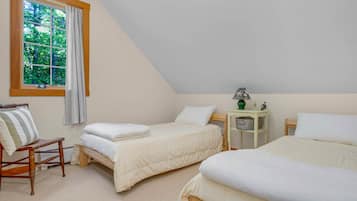 A bedroom with two beds, a window with curtains, a bedside table, and a chair.