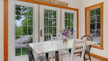A dining area with a white table and chairs, a vase with flowers, and a sign above the doors reading 'THE WHITE MOUNTAINS.'