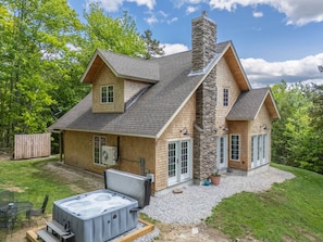 Une maison à deux étages avec une cheminée en pierre, un jacuzzi et une terrasse couverte.