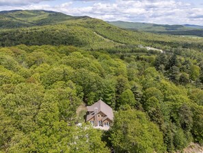 Una casa rodeada de un bosque denso y un paisaje montañoso al fondo.