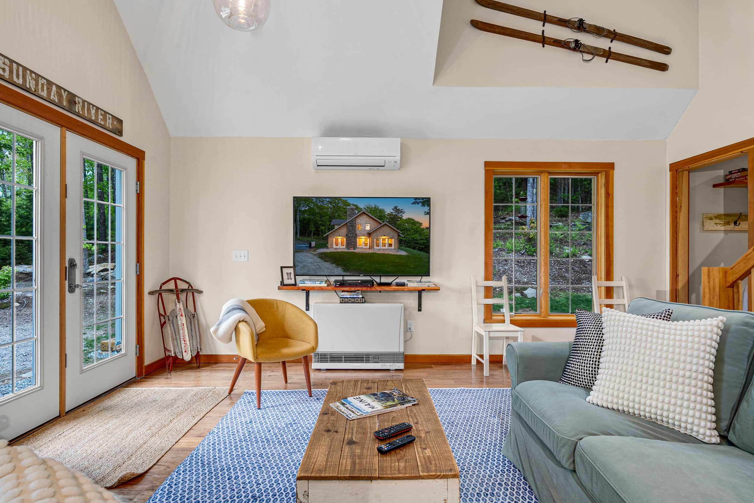 A living room with a TV, sofa, coffee table, and a view of a house through a large window.