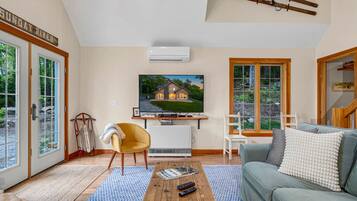 A living room with a TV, sofa, coffee table, and a view of a house through a large window.