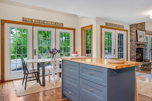 A kitchen with a large island, wooden cabinets, and a stone fireplace. - Sunday River|Mt Views| Dog Friendly|20% Off 3+ (Bryant Pond)