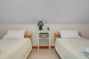 Une chambre double avec deux lits, une petite table avec une lampe et une étagère fixée au mur.