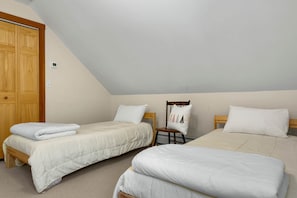 A bedroom with two beds, a wooden wardrobe, a chair, and a ceiling fan.