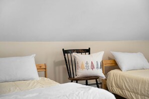Une chambre avec deux lits simples, une chaise en bois agrémentée d’un coussin décoratif et un mur sobre.