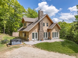 A two-story house with a stone chimney, large windows, and a covered patio area.