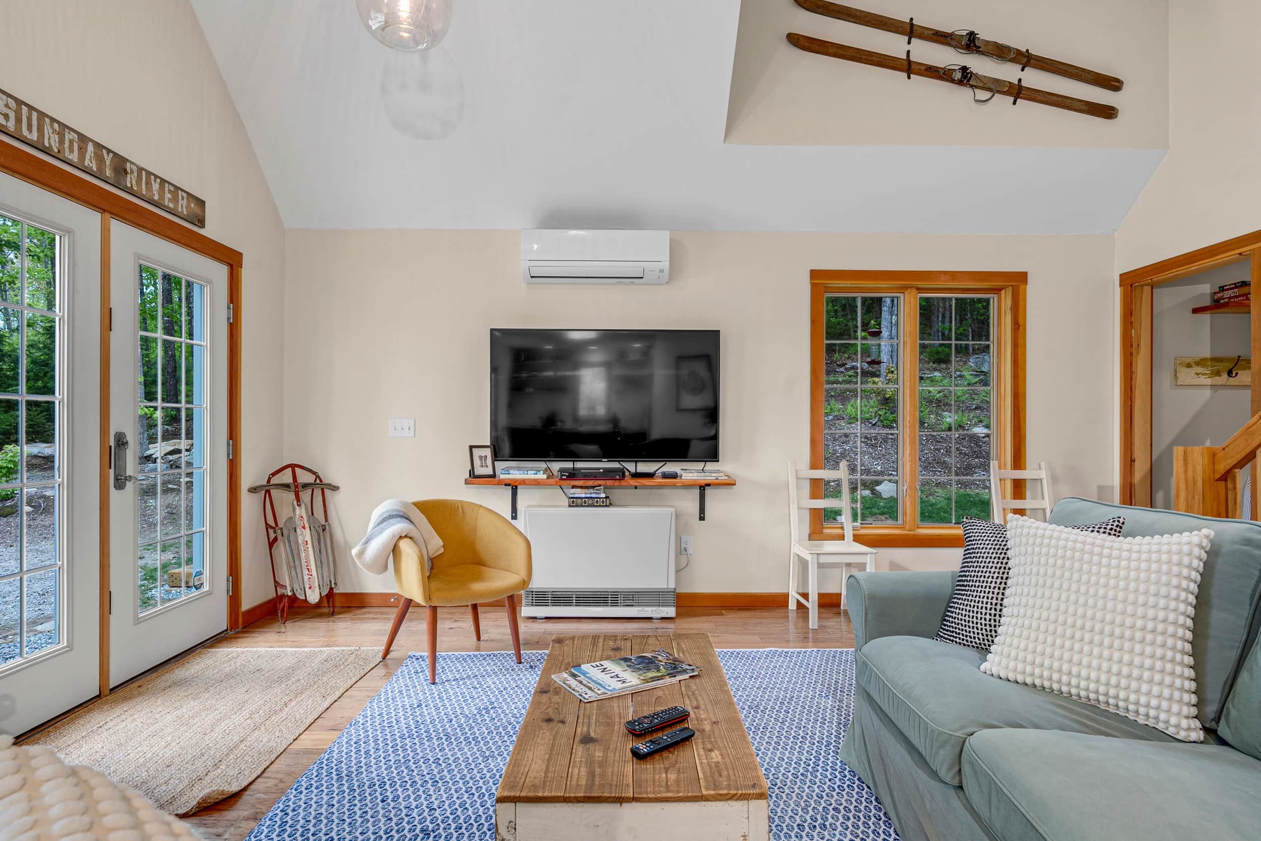 Sala de estar com televisão, sofá, mesa de centro e janela com vista para árvores.