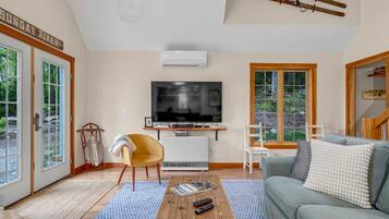 A living room with a television, a sofa, a coffee table, and a window with a view of trees.