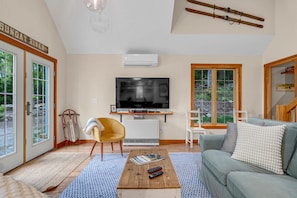 Una sala de estar con televisión, un sofá, una mesa de centro y una ventana con vistas a árboles.