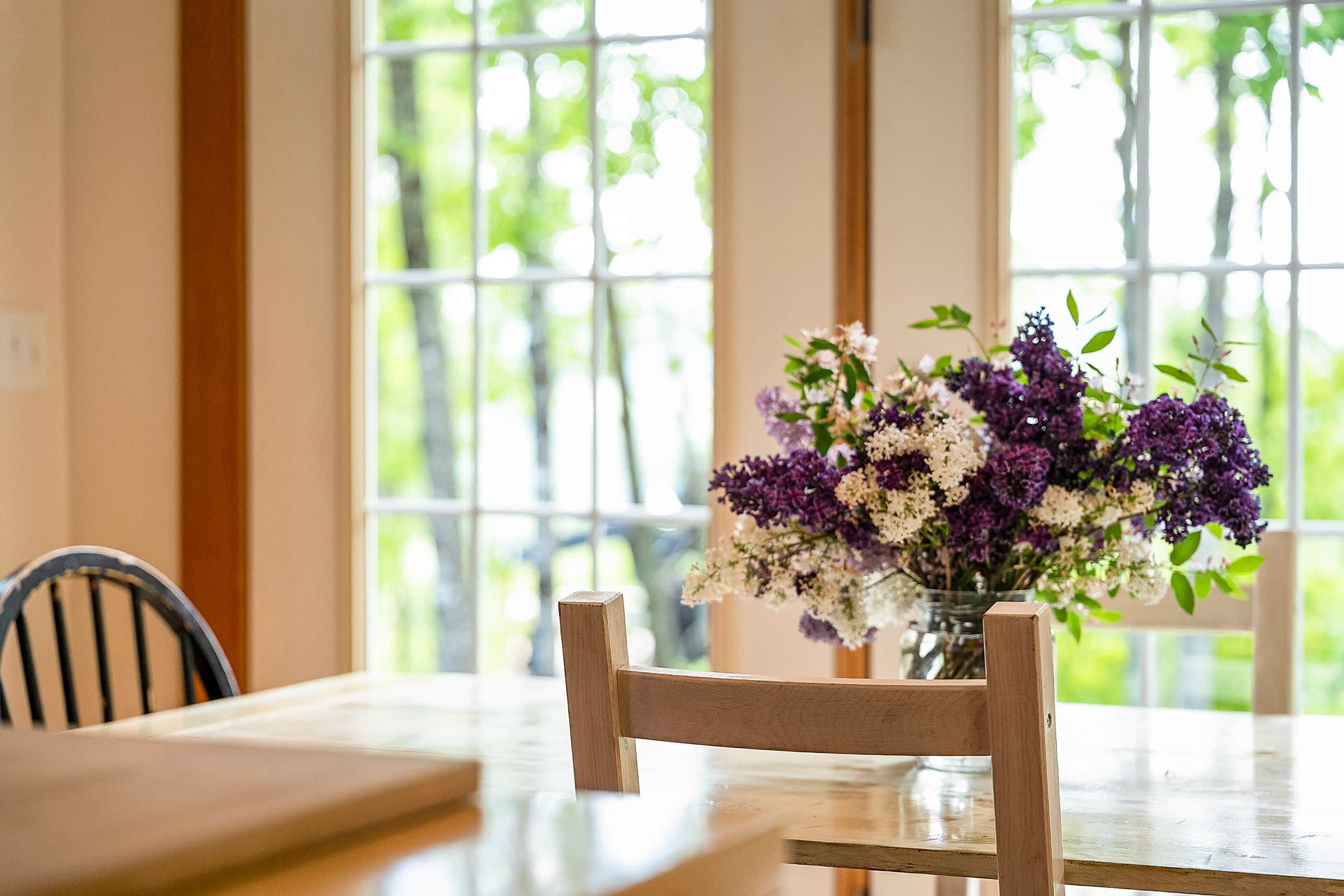 Una mesa de comedor con una silla de madera y un jarrón de flores.