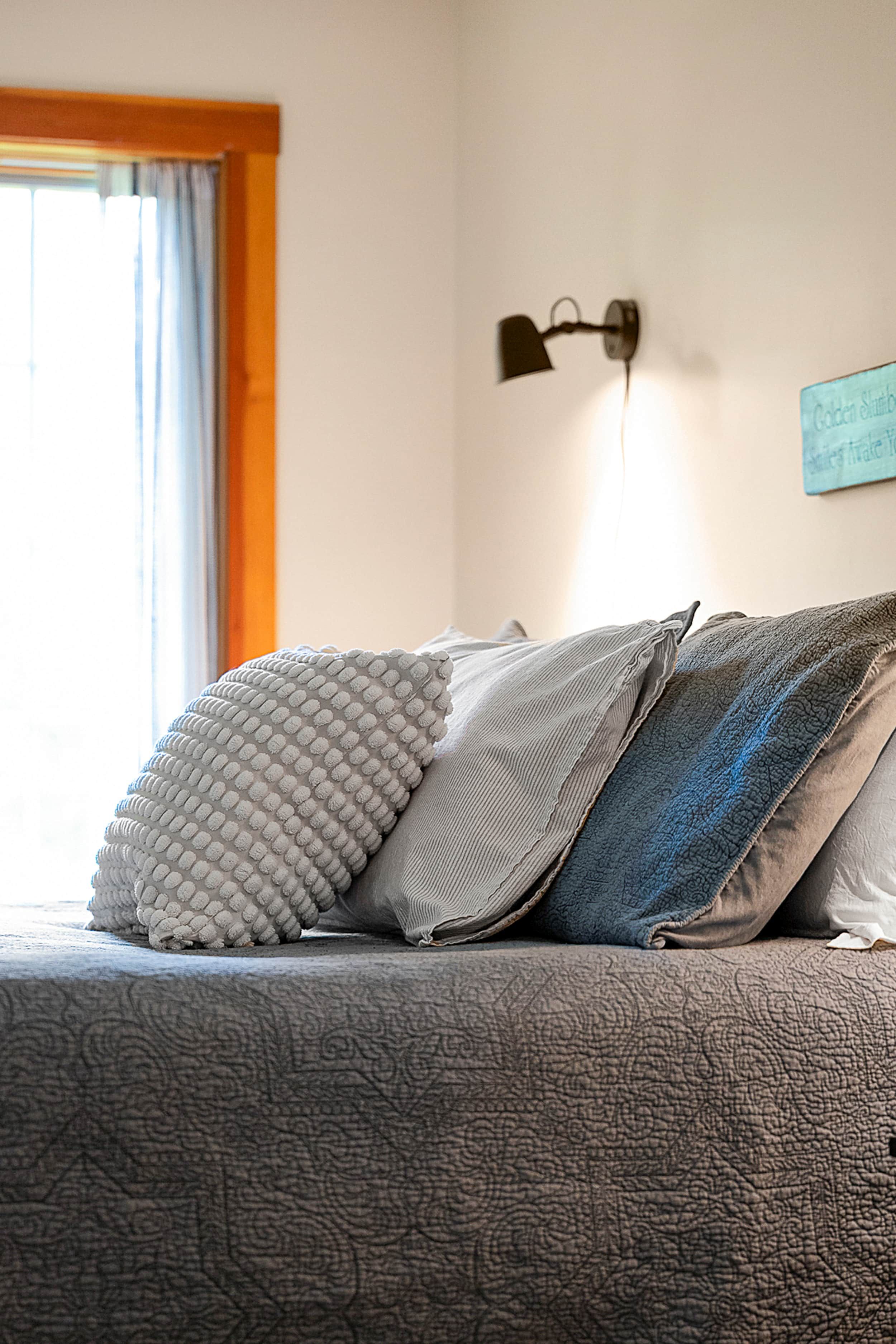 A bed with patterned bedding, a wall-mounted lamp, and a window with curtains.