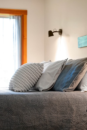 A bed with patterned bedding, a wall-mounted lamp, and a window with curtains. - Sunday River|Mt Views| Dog Friendly|20% Off 3+ (Bryant Pond)