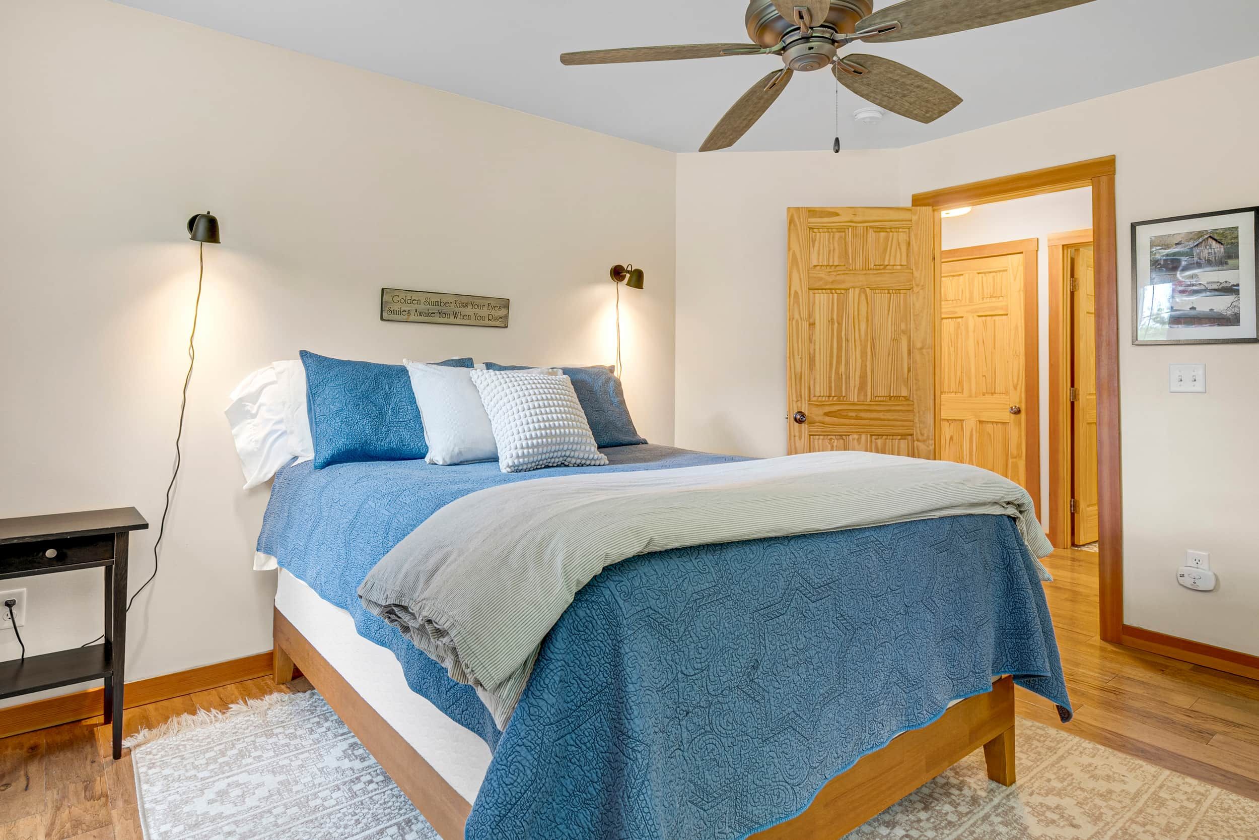 A bedroom with a bed, bedside lamps, a ceiling fan, and a wooden door.
