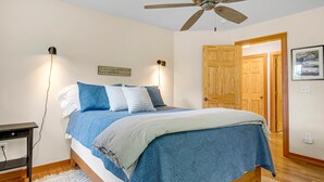 Un dormitorio con cama, lámparas de noche, ventilador de techo y una puerta de madera.