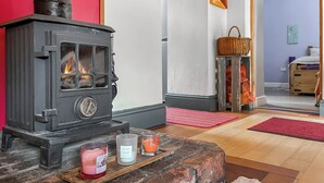 En vedeldad kamin med en röd lucka, en korg på en pall och ljus på ett fat.