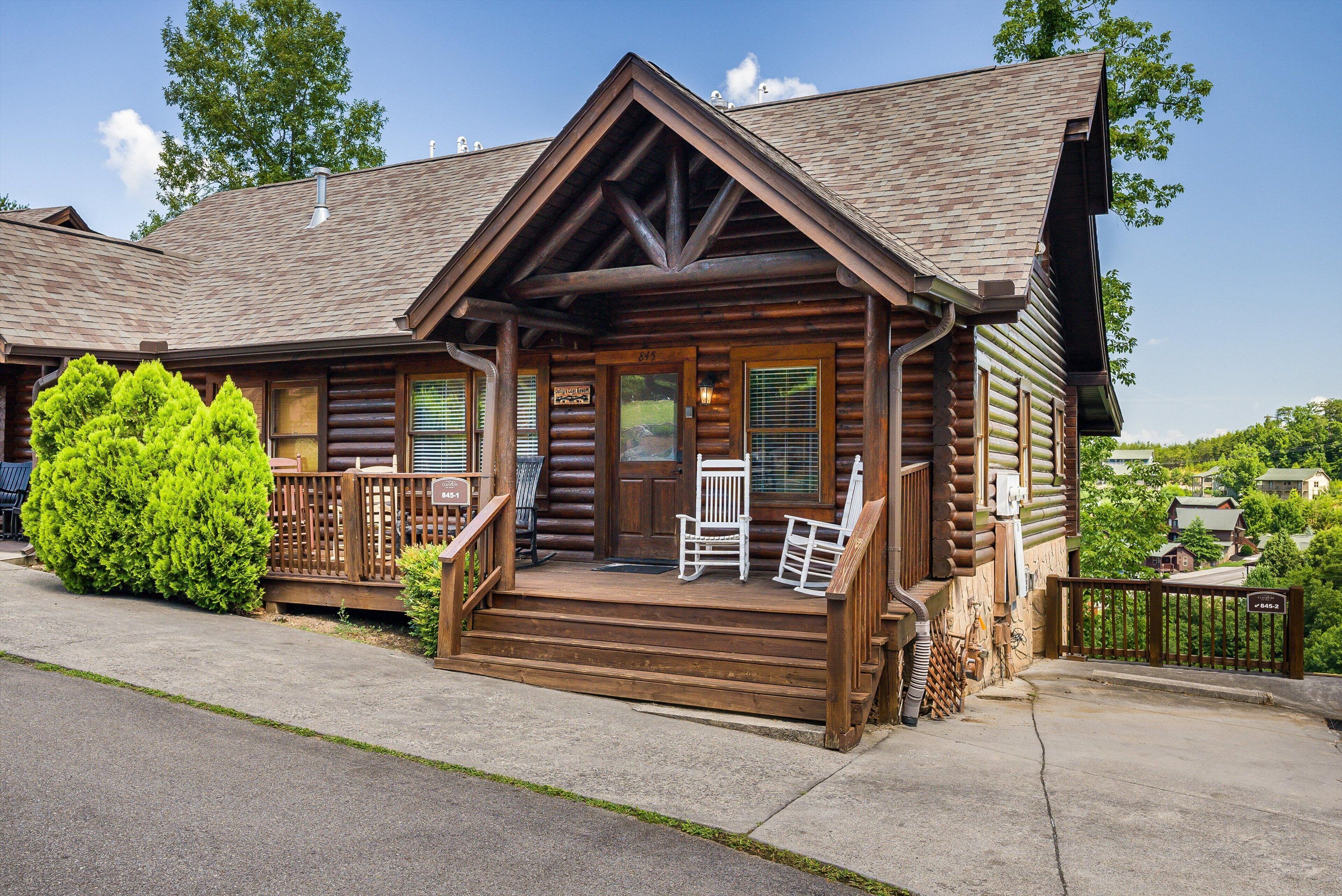 A log cabin with a porch, two rocking chairs, and a well-maintained lawn.