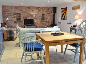 A cozy living room with a stone wall, a television, a fireplace, a dining table, and a sofa.