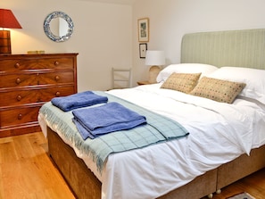 Quarto com cómoda de madeira, cama com roupa de cama branca e toalhas azuis, espelho e um quadro na parede.