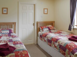 Une chambre à coucher avec deux lits simples, chacun agrémenté d’une courtepointe à motifs floraux, d’une tête de lit en bois et d’un petit tableau encadré accroché au mur.