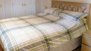 Una cama con una colcha escocesa, un cabecero de madera y una mesita de noche con una lámpara.