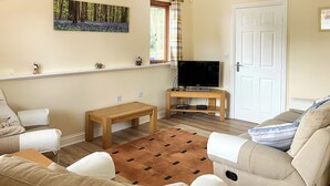 Una sala de estar con un sofá, una mesa de centro de madera, un televisor sobre un mueble bajo y un cuadro en la pared.