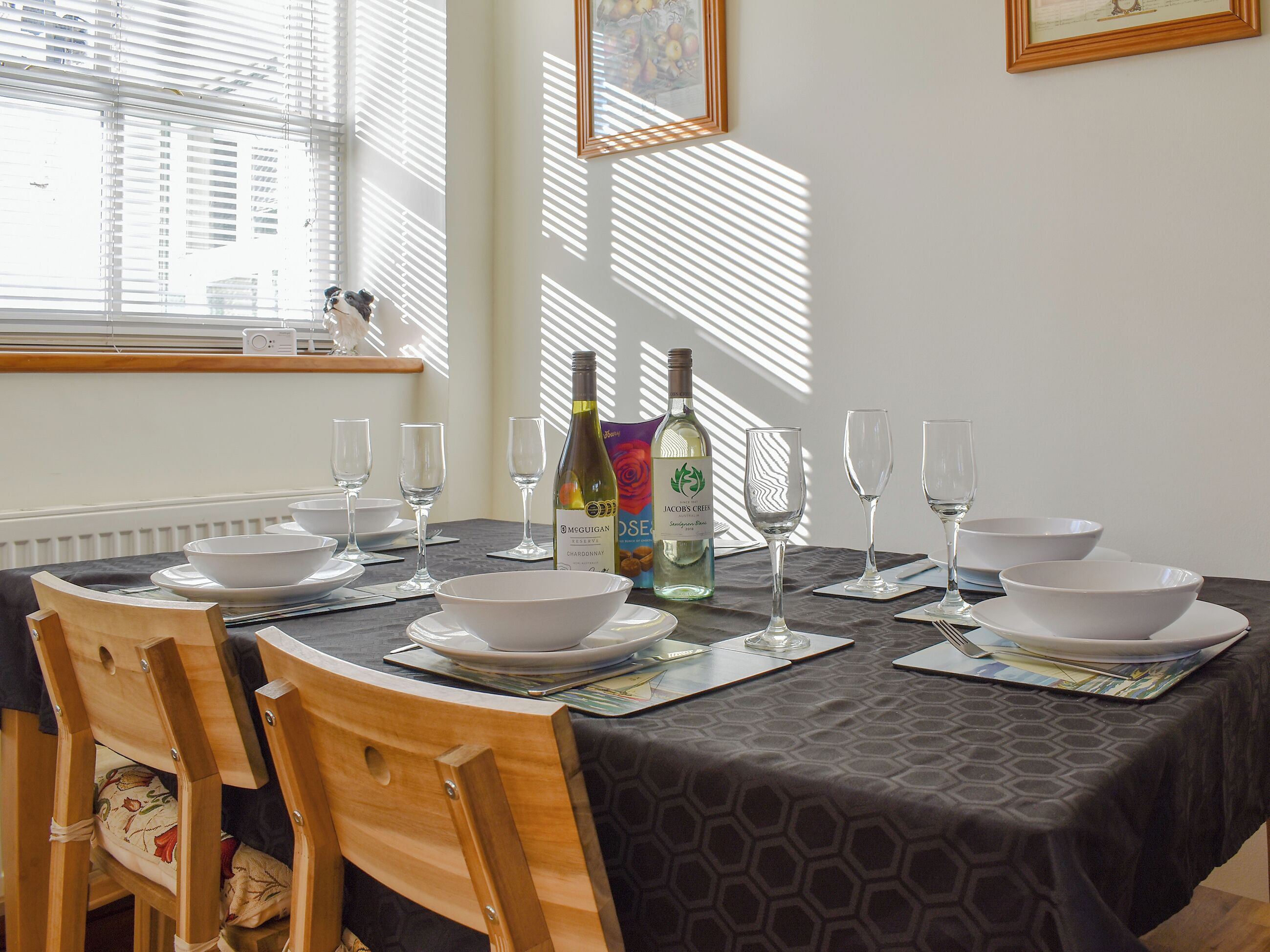 A dining table set with white bowls, plates, and wine glasses, a bottle of wine, and a menu.