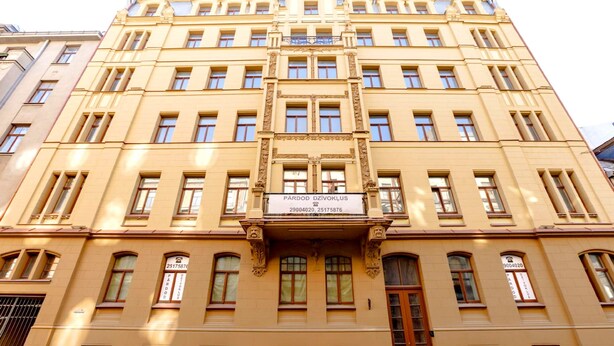 En bygning i flere etager med klassisk arkitektur, der har en central indgang med en dekorativ facade og adskillige vinduer på hver etage.