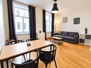 A modern living room with a sofa, a dining table with chairs, a coffee table, a floor lamp, and a potted plant.