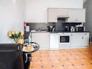 A compact kitchen with white cabinets, a black countertop, a dishwasher, an oven, and a tiled floor.