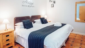 A neatly made bed with a dark blue bedspread, white pillows, and a wall-mounted sign that reads 'Always kiss me goodnight...'. - Gardener's Cottage - UK6713 (Lydstep, near Tenby)