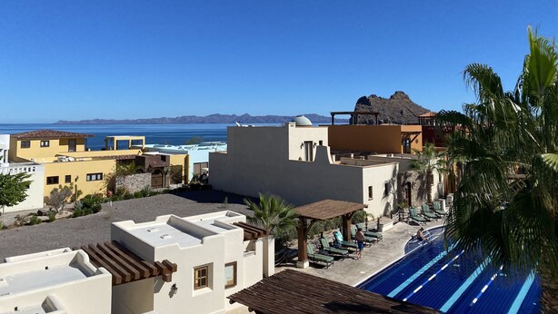 Un hôtel en bord de mer, doté d’une piscine, de palmiers et offrant une vue sur l’océan.