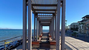 Une allée couverte, bordée de colonnes et de bancs, qui mène à un plan d’eau.