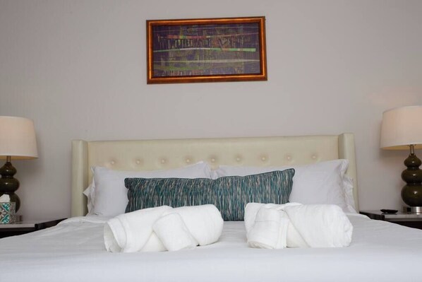 A hotel room with a bed, two pillows, a framed artwork, and two bedside lamps.