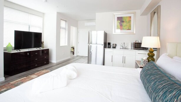 Una habitación de hotel con una cama grande, un televisor en una cómoda, una kitchenette y un baño.