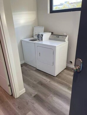 A compact laundry room with a washing machine and dryer, wooden flooring, and a window providing natural light.