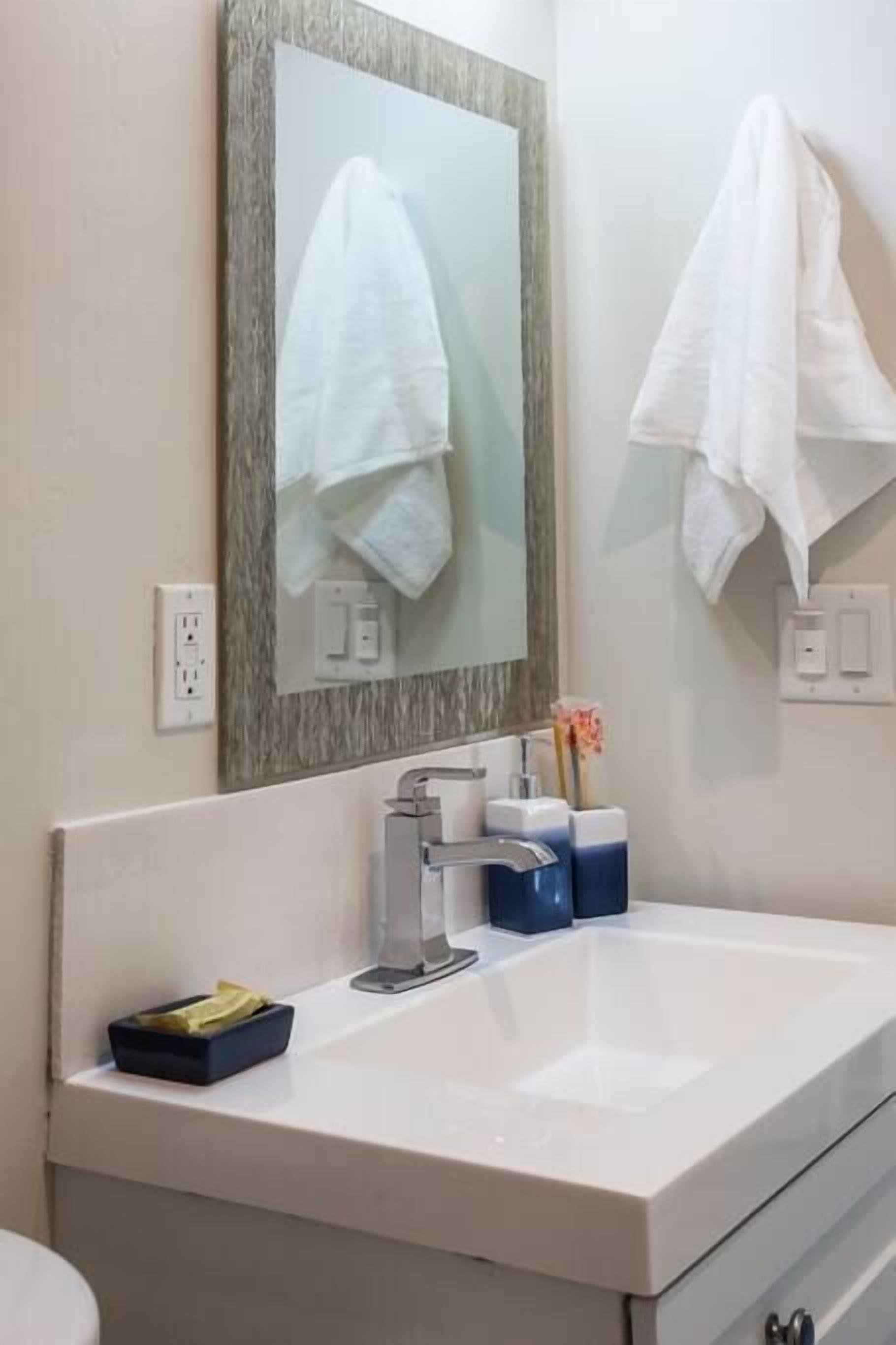 Une salle de bain avec un lavabo blanc, un miroir avec un cadre en bois et deux serviettes blanches accrochées au mur.