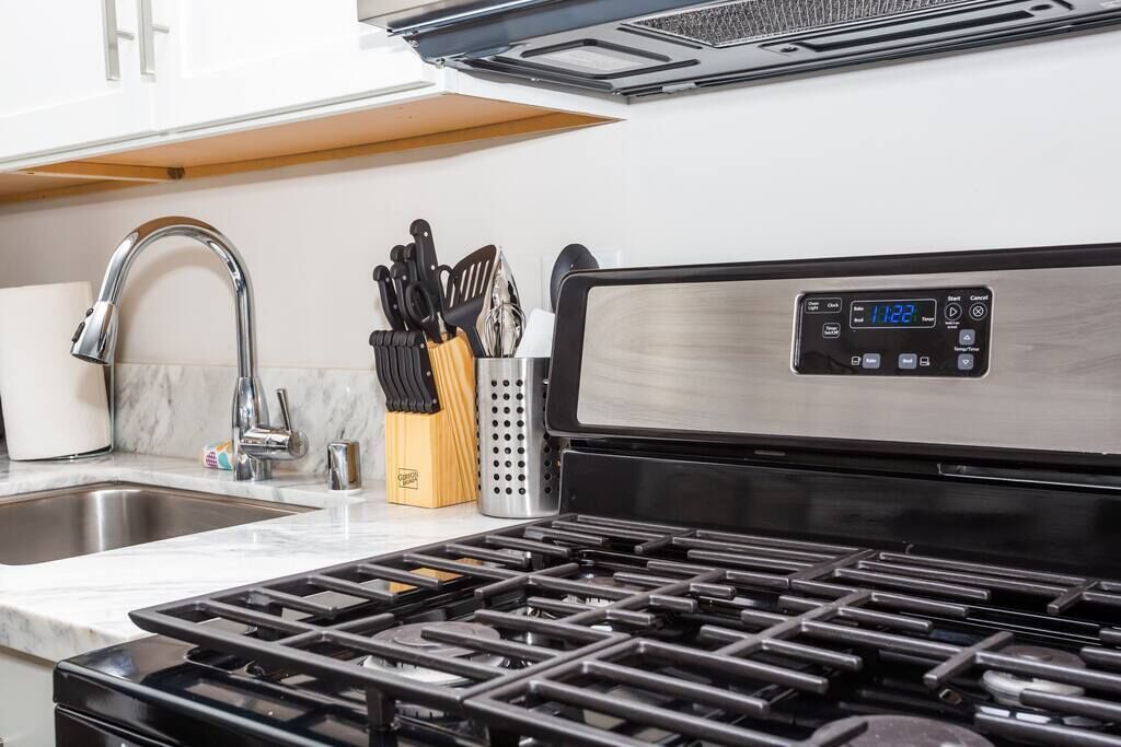 A kitchen with a stainless steel stove, a sink, and a knife block.