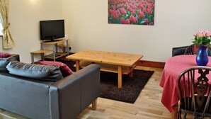A living room with a sofa, a wooden table, a TV, and a painting of tulips. - 1 bedroom accommodation in Belford near Bamburgh (Belford near Bamburgh)